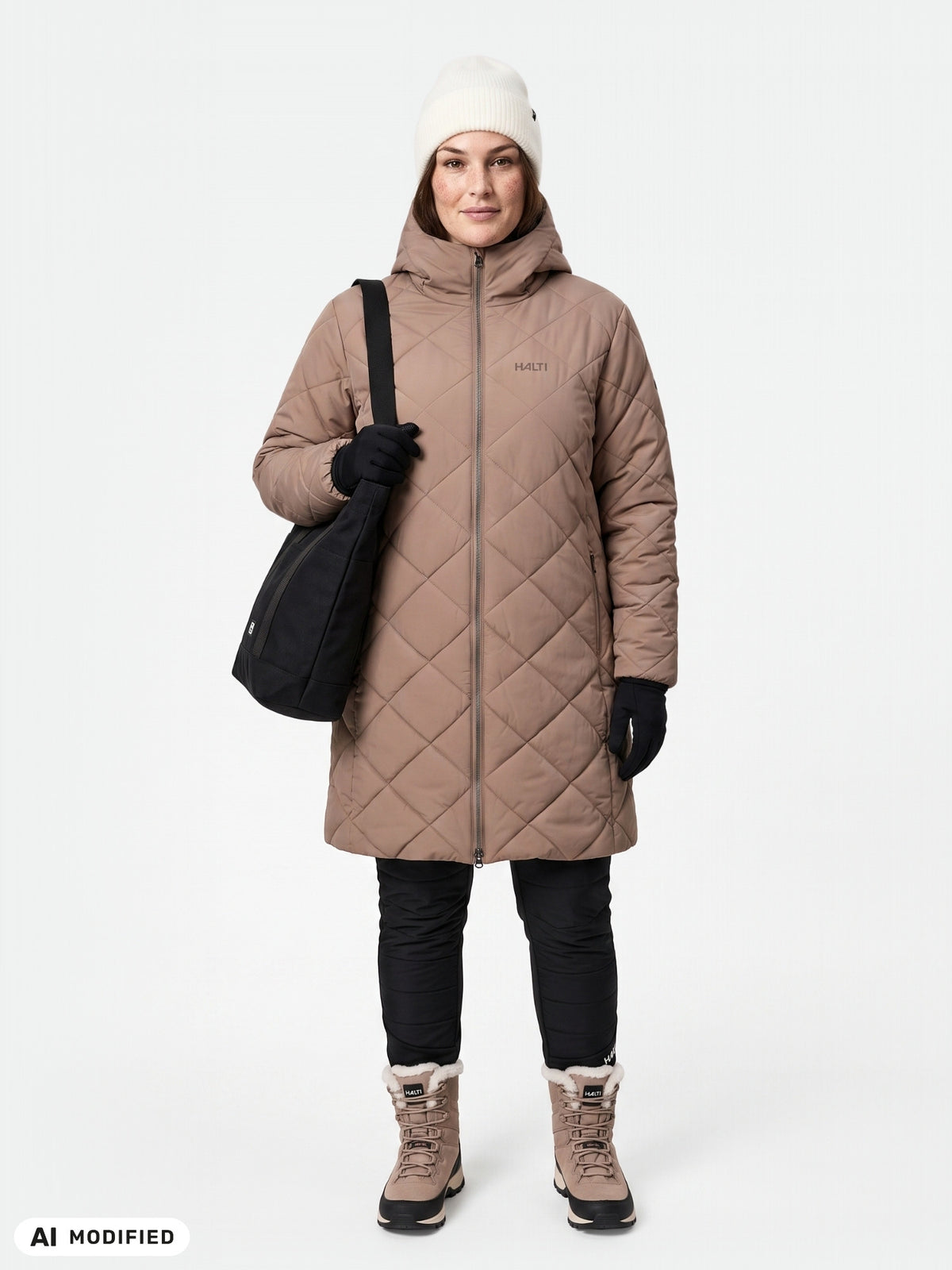 Eine Person in einem beigen Halti Haapa Steppmantel für Damen in Übergröße mit Kapuze, schwarzer Hose, Stiefeln, weißer Mütze, Handschuhen und einer Tasche.