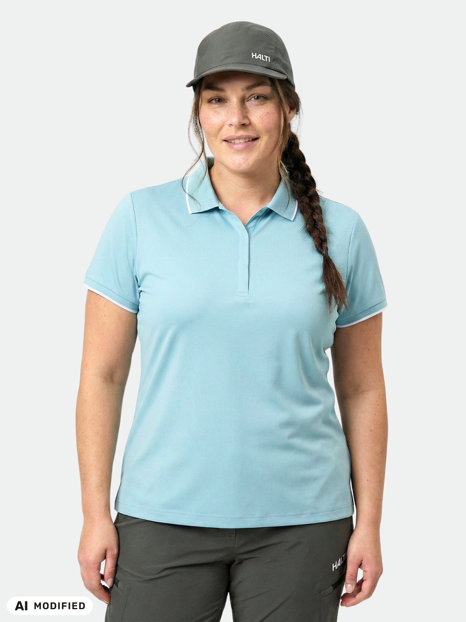 Frau in einem „Halti Swingi“ Technical-Poloshirt für Damen in Übergröße, einer dunklen Hose und einer grauen Mütze vor weißem Hintergrund.