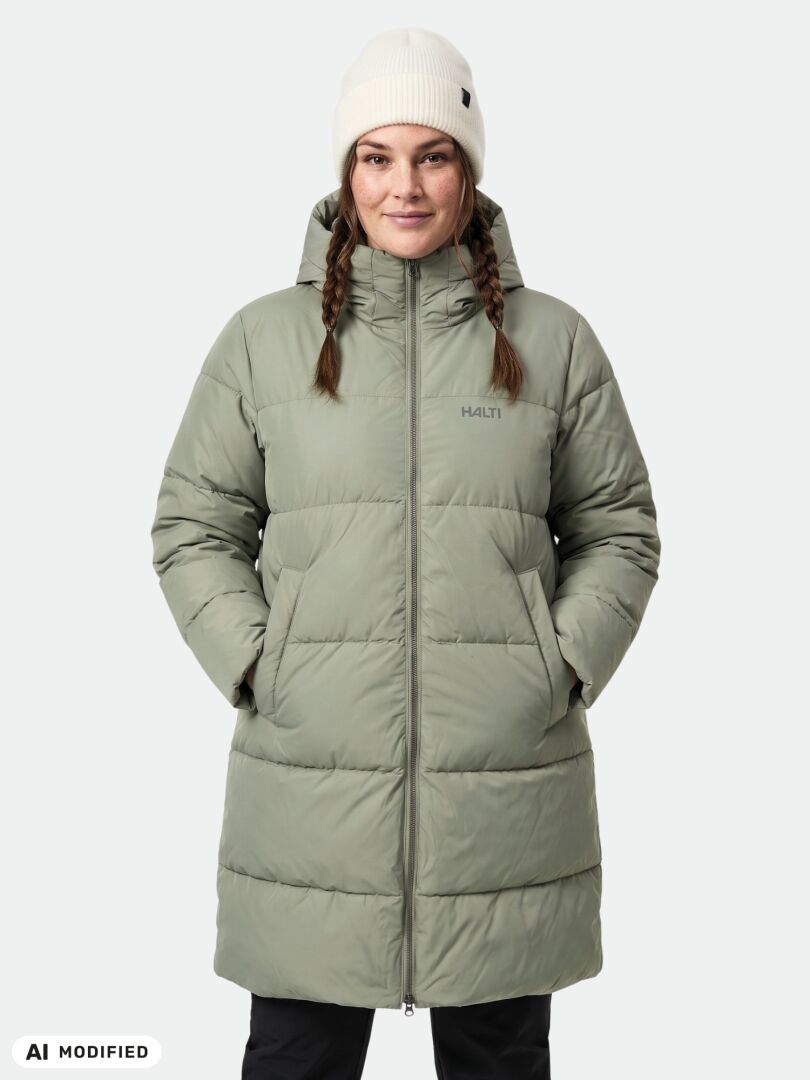 Person im „Halti Sammal II Plus-Size“-Isolationsparka, hellgrün mit Kapuze, und einer weißen Strickmütze, vor einfarbigem Hintergrund.