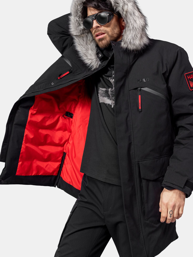 Ein Mann in einem Halti 1976 Daunenparka Unisex mit pelzgefütterter Kapuze zeigt sein rotes Futter und trägt eine Sonnenbrille.