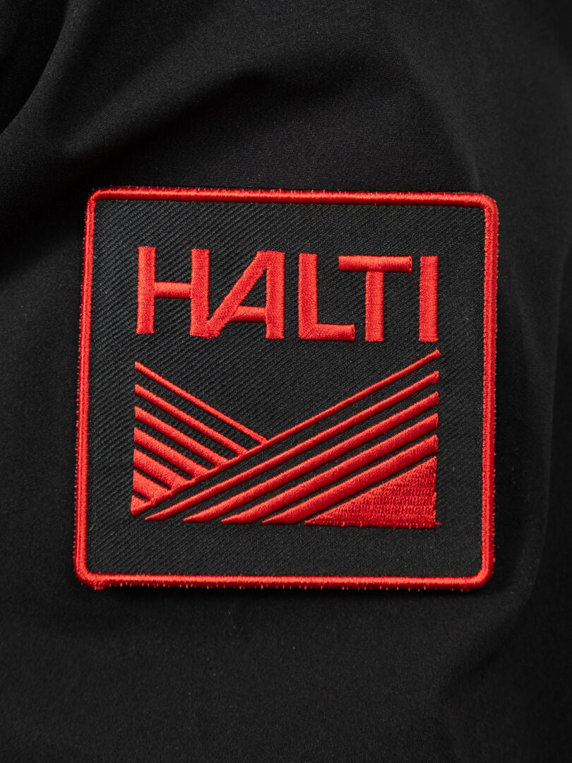 Ein rot-schwarzer HALTI-Aufnäher, inspiriert vom finnischen Design, auf schwarzem Stoff für den Halti 1976 Down Parka Unisex.