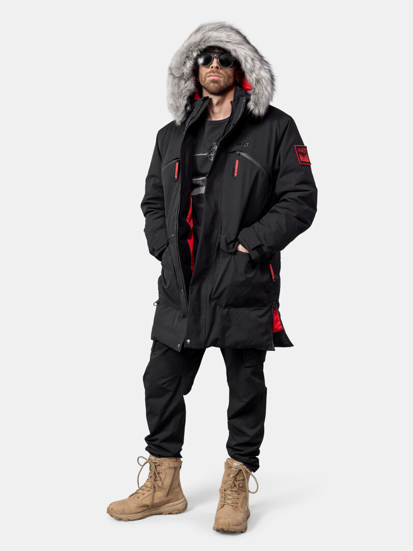 Eine Person, die einen Halti 1976 Down Parka Unisex, eine schwarze Hose, hellbraune Stiefel und eine Sonnenbrille trägt.