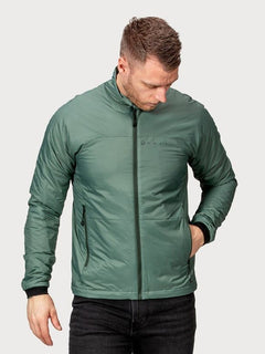 Ein Mann in grüner Halti Neon Primaloft Kunstfaserjacke Herren und schwarzer Hose steht mit einer Hand in der Tasche und schaut nach unten.