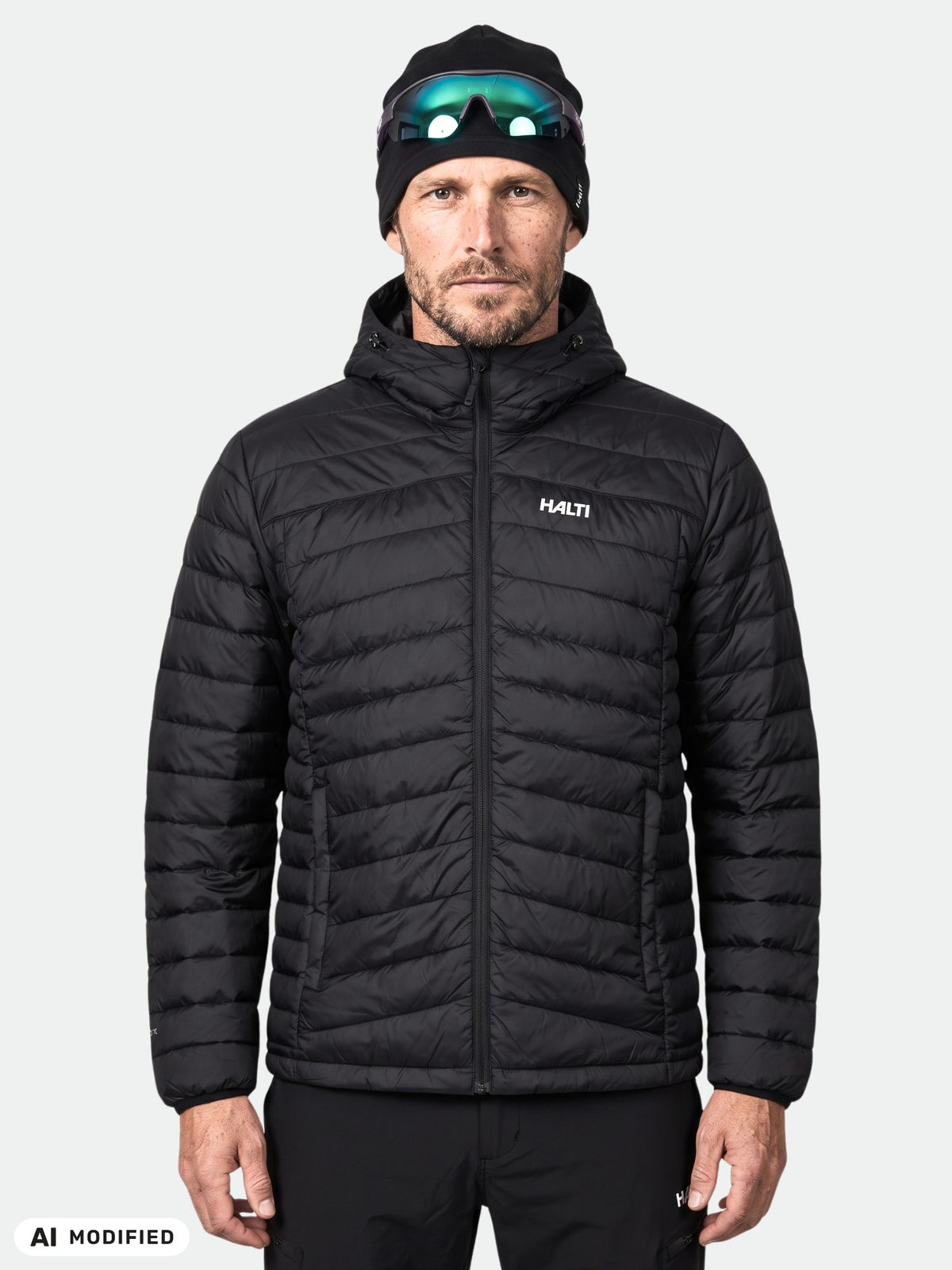 Ein Mann, der eine schwarze Halti Huippu Daunenjacke Herren-Daunenjacke, eine Mütze und eine Sonnenbrille auf der Stirn trägt.