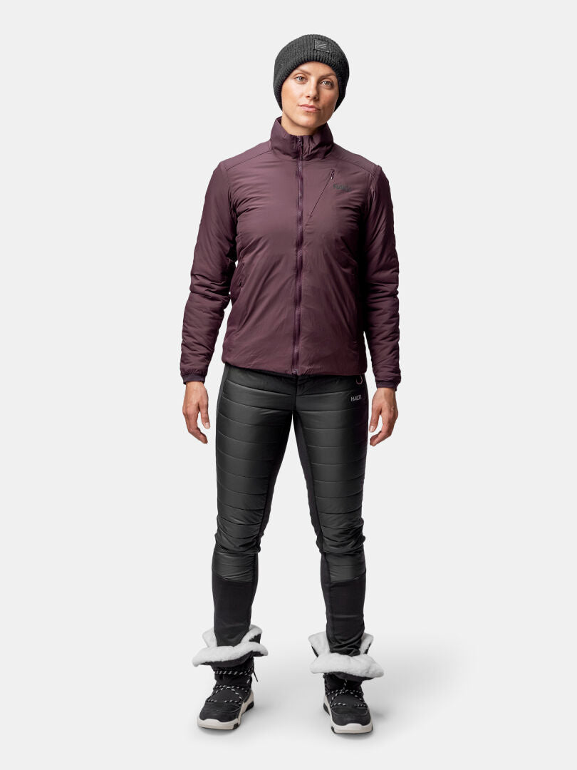 Eine Frau in einer Halti Haave Insulation Primaloft Jacke Damen, einer schwarzen Hose, Stiefeln und einer grauen Mütze sieht nach vorne.