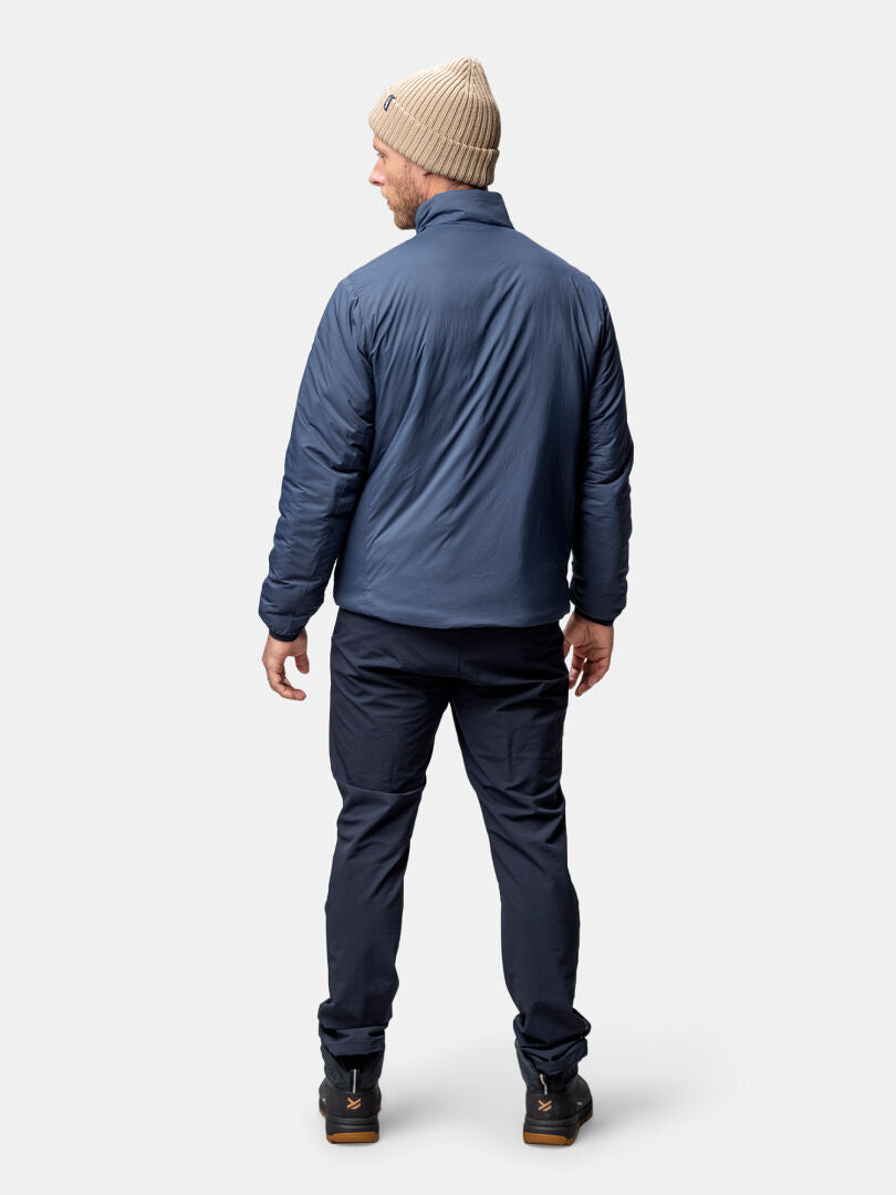 Ein Mann in einer blauen Halti Haave Insulation Primaloft Jacke Herren steht mit dem Gesicht nach außen, bereit für Aktivitäten im Freien.