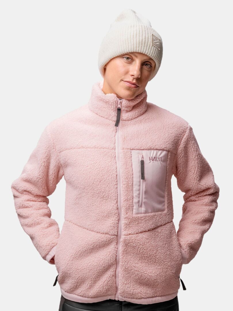 Person, die eine blassrosa Fleecejacke und die Halti Huurre Mütze trägt, Hände in den Jackentaschen.