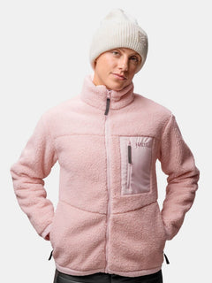 Person, die eine blassrosa Fleecejacke und die Halti Huurre Mütze trägt, Hände in den Jackentaschen.