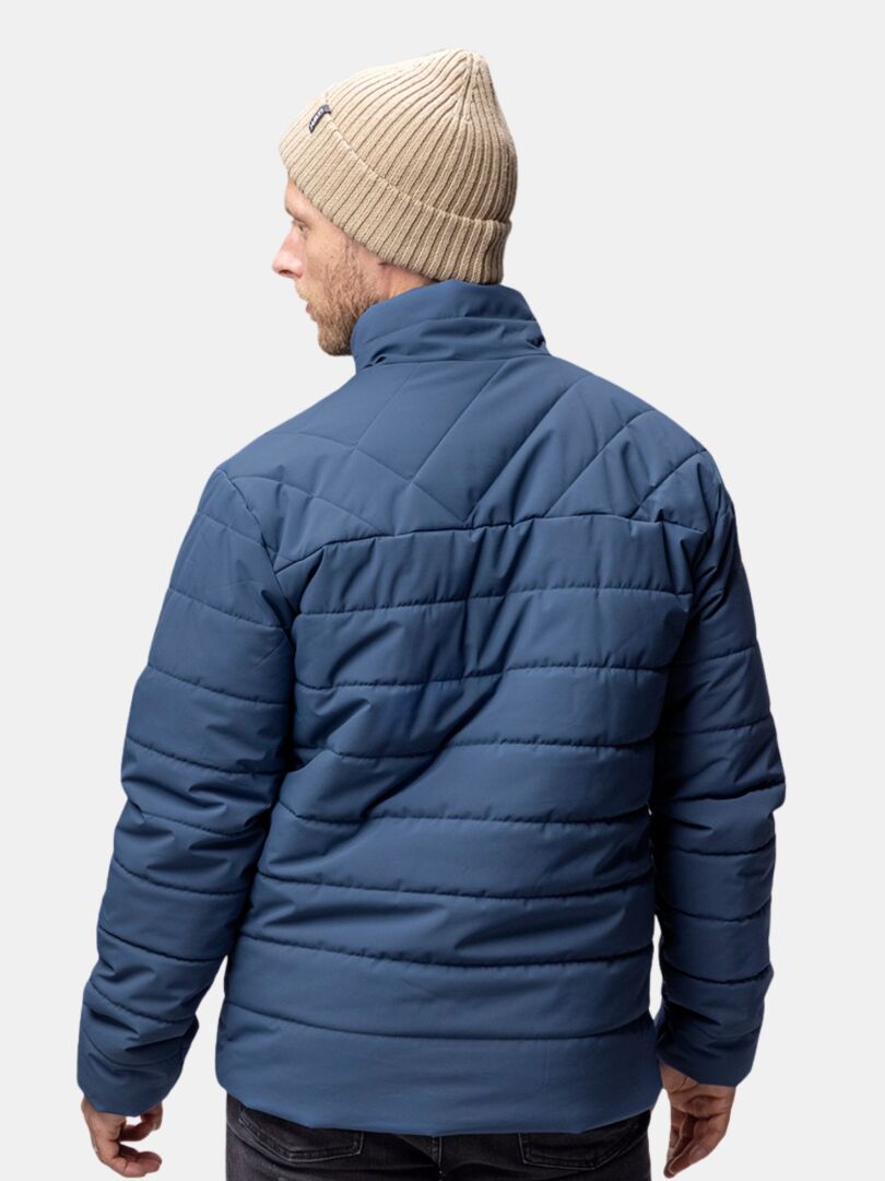 Ein Mann in einer beigen Halti Runko Mütze und einer blauen Steppjacke ist von hinten vor einem schlichten hellen Hintergrund zu sehen.