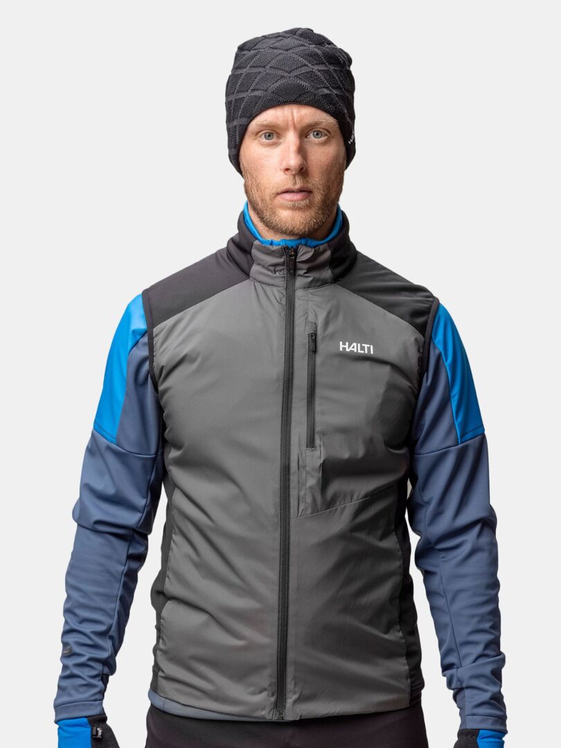 Ein Mann in einer winddichten grau-blauen Jacke, passenden Handschuhen und einer Halti Crostie Merino Mütze steht mit dem Gesicht nach vorne.