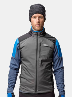 Ein Mann in einer winddichten grau-blauen Jacke, passenden Handschuhen und einer Halti Crostie Merino Mütze steht mit dem Gesicht nach vorne.