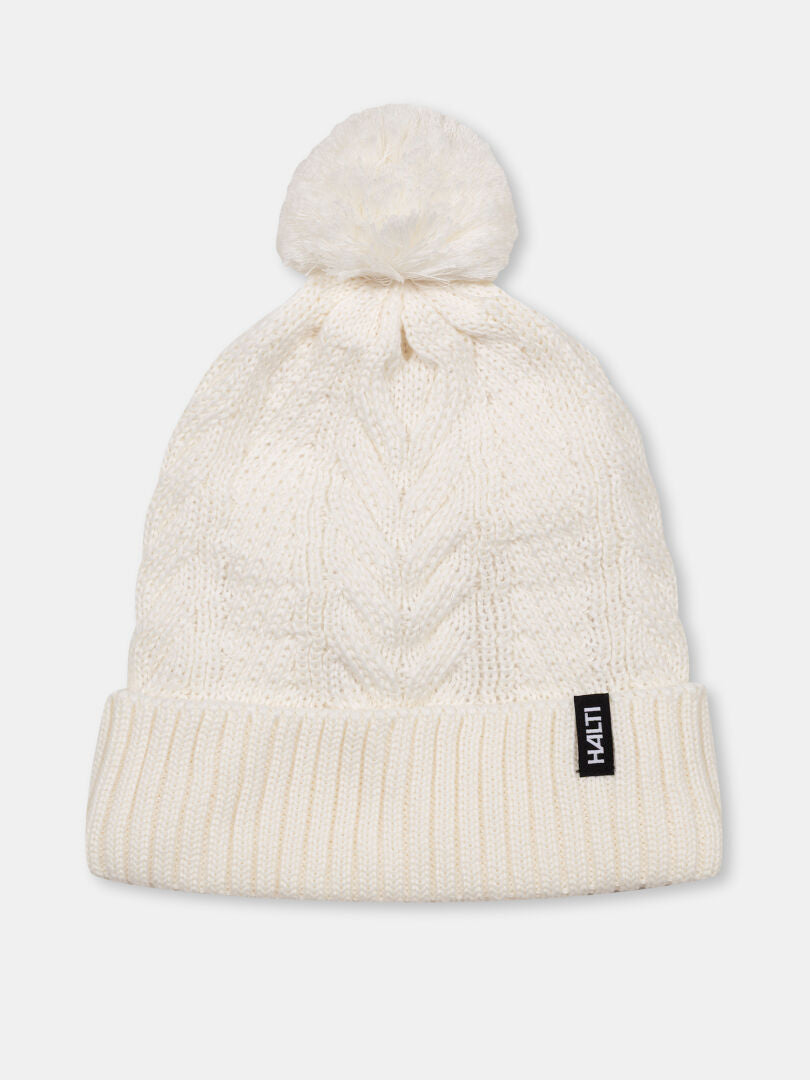 Die Halti Hile Mütze ist weiß, mit Zopfmuster, Pom-Pom, Fleecefutter und schwarzem LIVHAT-Label am Rand.