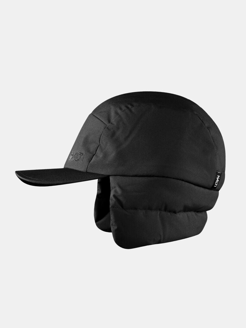Die Halti Huove Puffy Hut ist eine schwarze Wintermütze mit Ohrenklappen, die vor einem hellgrauen Hintergrund abgebildet ist.