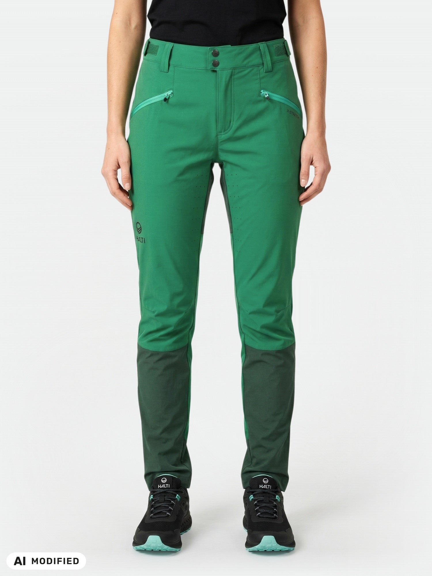 Eine Person trägt eine grüne „Halti Tracks Damen X-Stretch“-Hose und schwarze Schuhe und steht vor einem weißen Hintergrund.