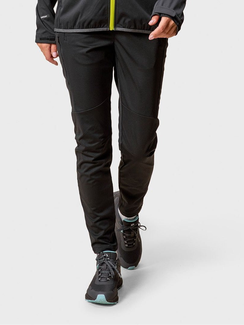 Sie trägt Halti Exhale Stormwall Hosen Damen, eine schwarze Jacke und tealfarbene Turnschuhe und geht vorwärts.