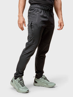 Ein Mann in Halti Exhale Stormwall Hosen und Hemd, mit hellgrünen Sportschuhen, steht vor einem schlichten Hintergrund.