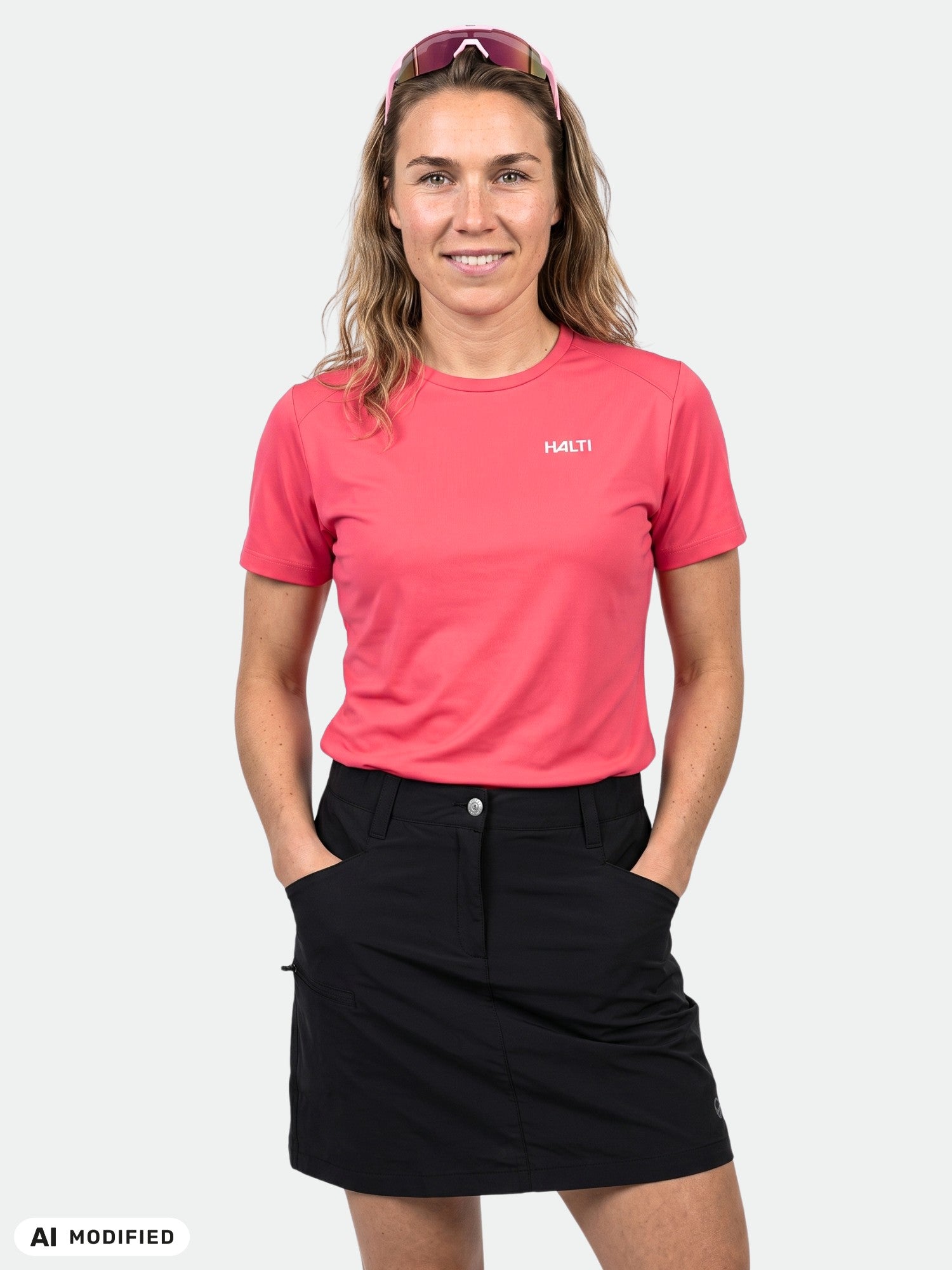 Eine Person in einem rosa „Halti Salves“-T-Shirt für Damen und einem schwarzen Rock steht mit den Händen in den Taschen vor einem schlichten Hintergrund.