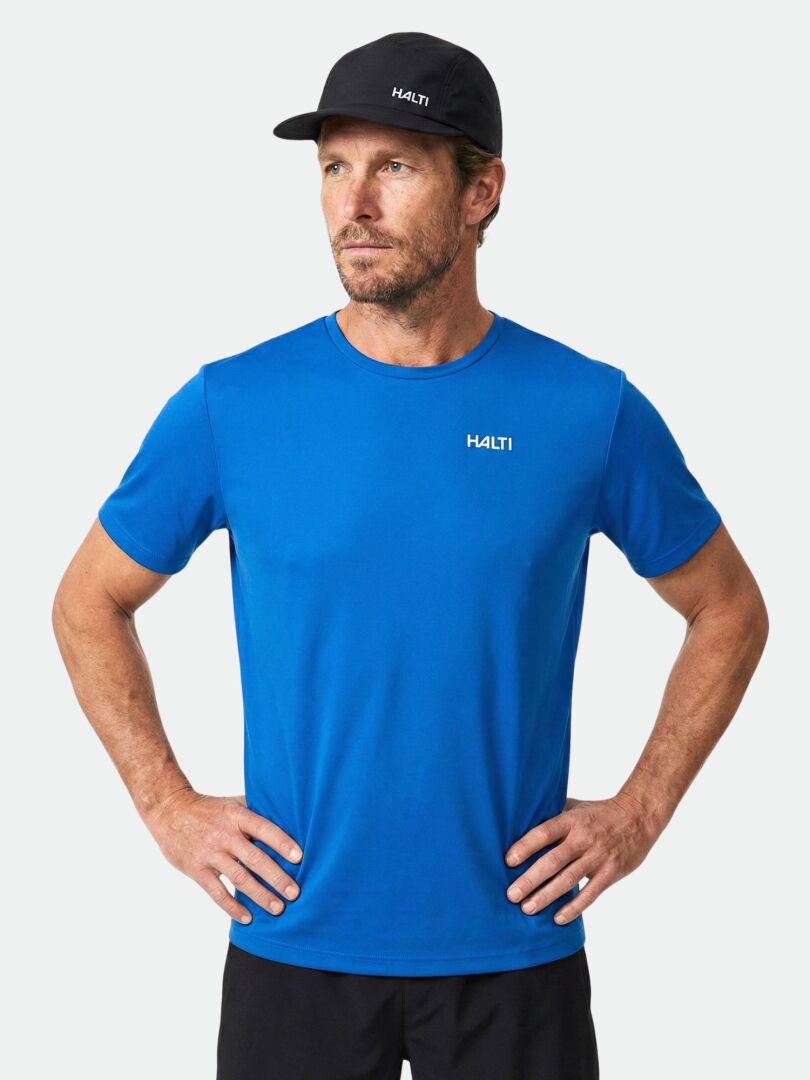Ein Mann in einem blauen Halti Salves T-Shirt Herren und einer schwarzen Halti-Mütze steht mit den Händen in den Hüften und schaut nach rechts.