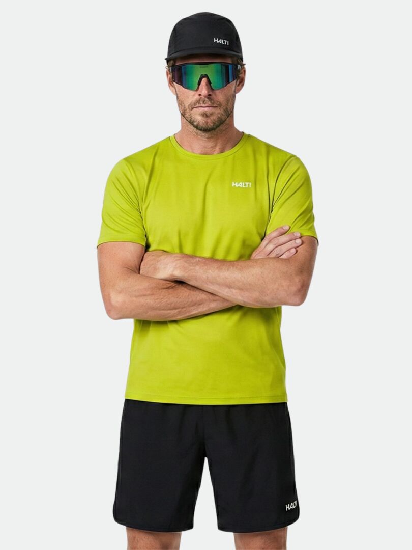 Mann in Halti Salves T-Shirt Herren, schwarzen Shorts, Mütze und reflektierender Sonnenbrille steht mit verschränkten Armen.
