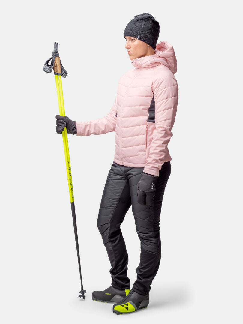 Person in Wintersportkleidung mit gelben Skistöcken, trägt Halti Hanki 2 Hybrid Langlaufjacke Damen und schwarze Hose.