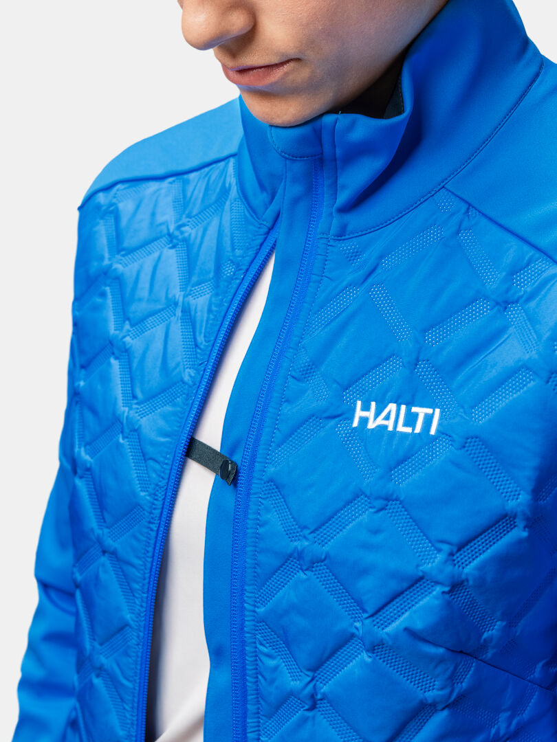 Person in einer hellblauen Halti Framover Hybrid Langlaufjacke Damen, teilweise ohne Reißverschluss, Brustlogo sichtbar.