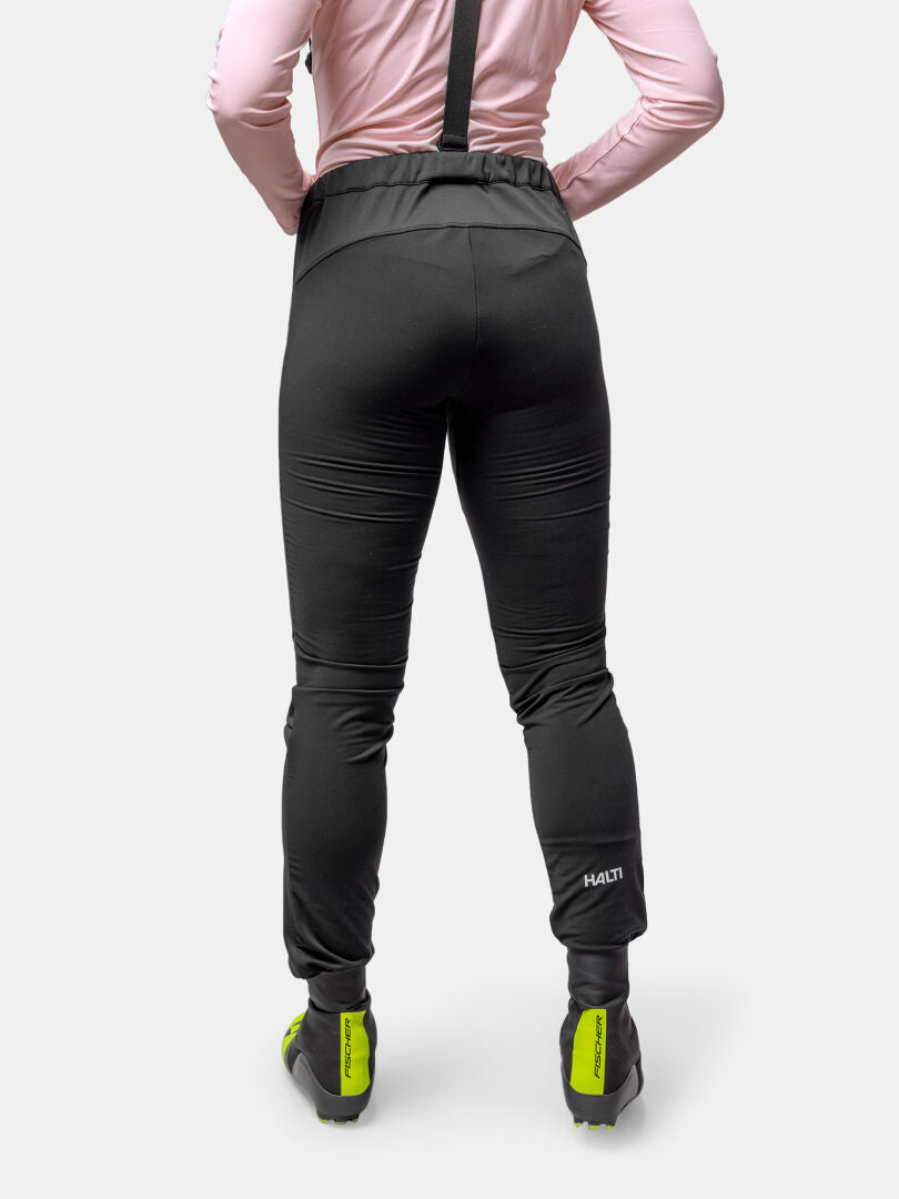 Rückenansicht einer Frau in Halti Huuru Langlaufanzug, rosa Top und neongelben Schuhen - perfekt für das Wintertraining.