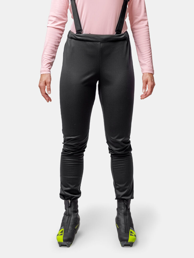 Eine Person in einem Halti Huuru Langlaufanzug Damen trägt eine schwarze Latzhose, ein pinkfarbenes langärmeliges Oberteil und schwarze Fahrradschuhe.