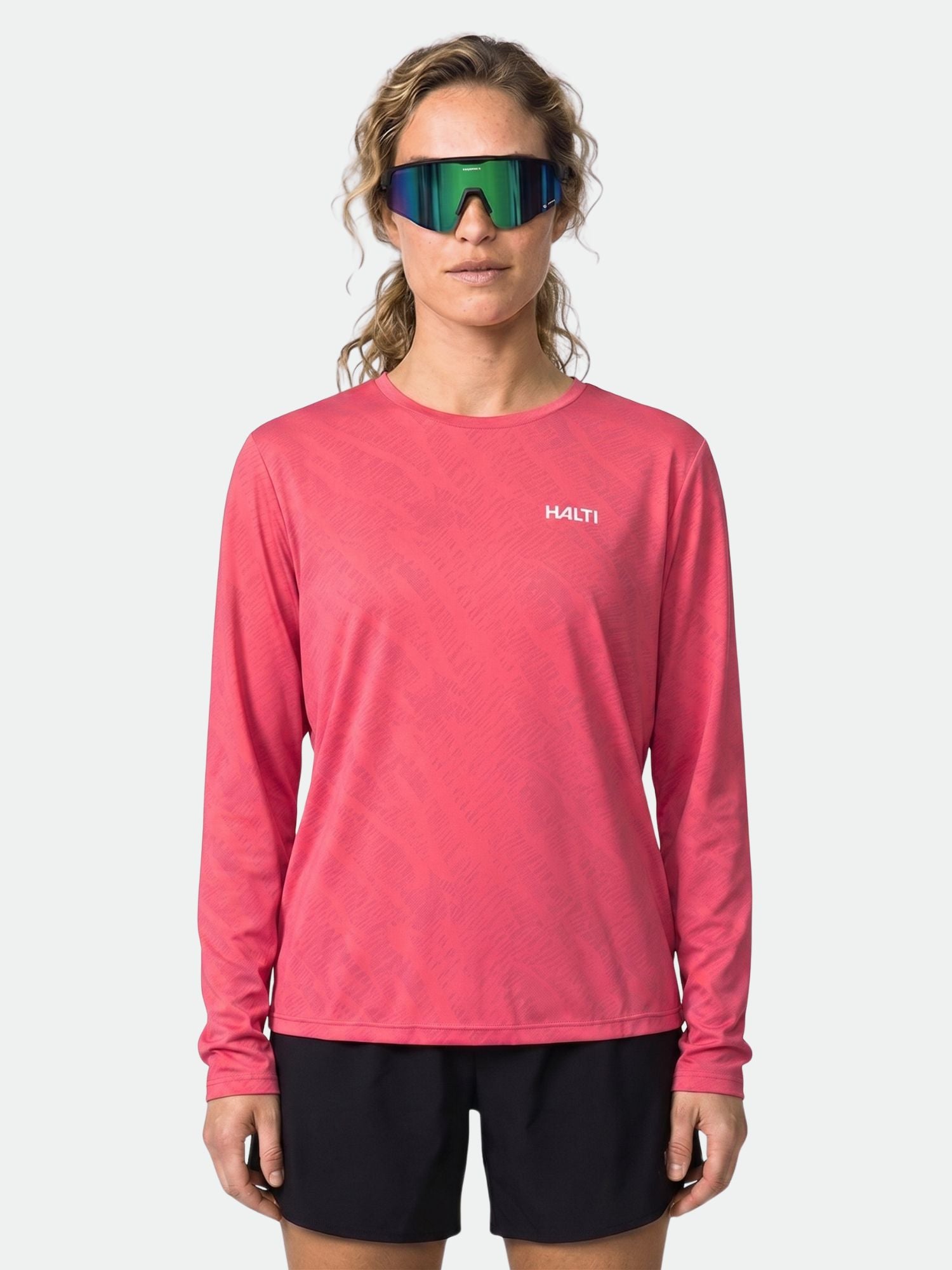 Eine Frau in einem rosa Halti Oulanka Trainingsshirt Damen mit UPF 50+ und schwarzen Shorts trägt eine reflektierende Sport-Sonnenbrille.