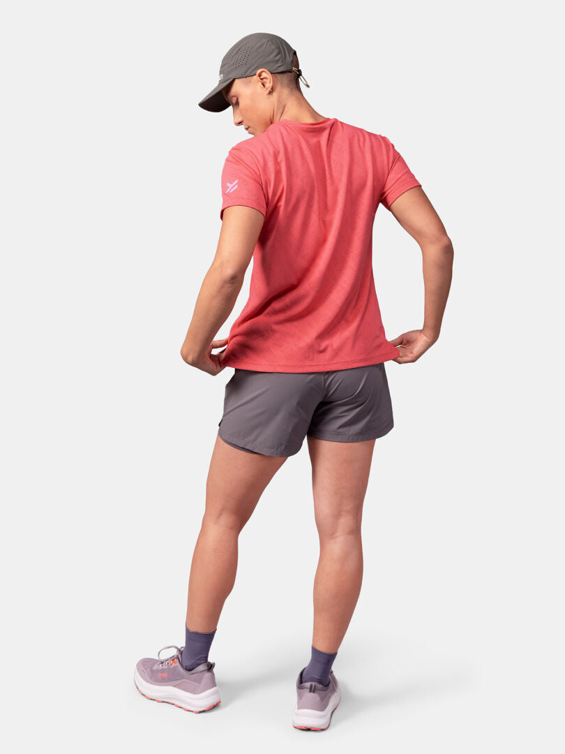 Eine Person in einem roten Halti Oulanka T-Shirt Damen, grauen Shorts und Mütze steht im Freien und schaut von der Kamera weg.