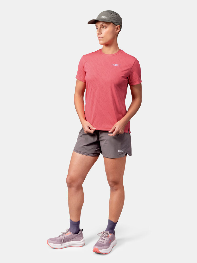 Frau im Halti Oulanka T-Shirt Damen, grauen Shorts und Hut beim Outdoor-Training vor weißem Hintergrund.