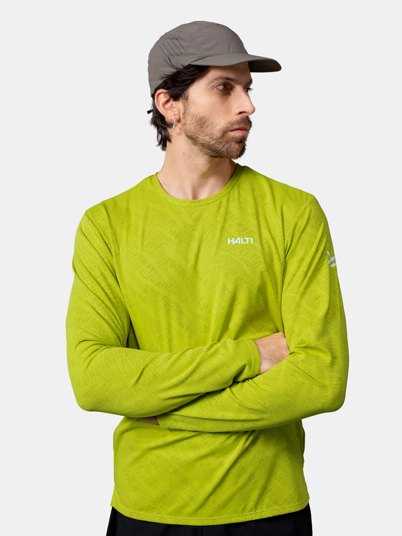 Mann mit grauer Mütze und hellgrünem Halti Oulanka Trainingsshirt Herren, Arme verschränkt, schaut zur Seite.