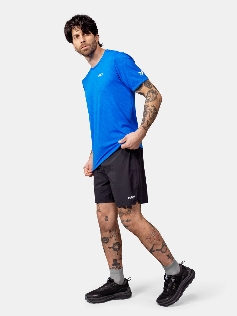 Ein Mann, der das Halti Oulanka T-Shirt Herren, schwarze Shorts und Turnschuhe trägt, posiert vor einem weißen Hintergrund.