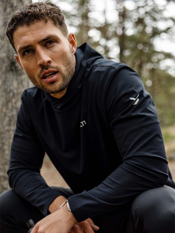Ein Mann, der Halti Kaltio Trainingshoodie Herren trägt, sitzt im Freien in einem bewaldeten Gebiet und schaut mit einem neutralen Blick nach oben.