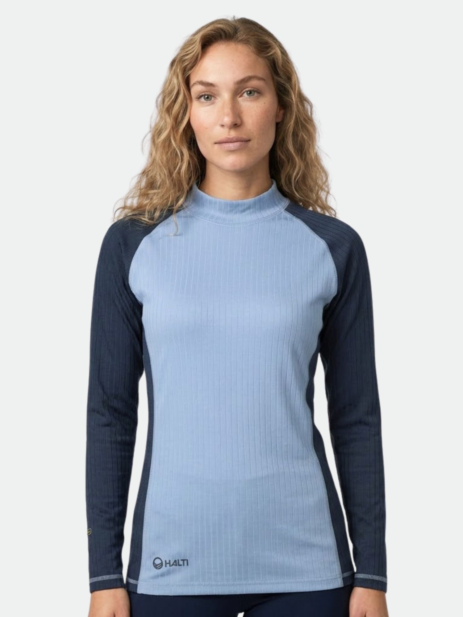 Eine Person mit gewelltem Haar modelliert das Halti Baselayer Set Damen in Hellblau und Marineblau vor einem schlichten Hintergrund.