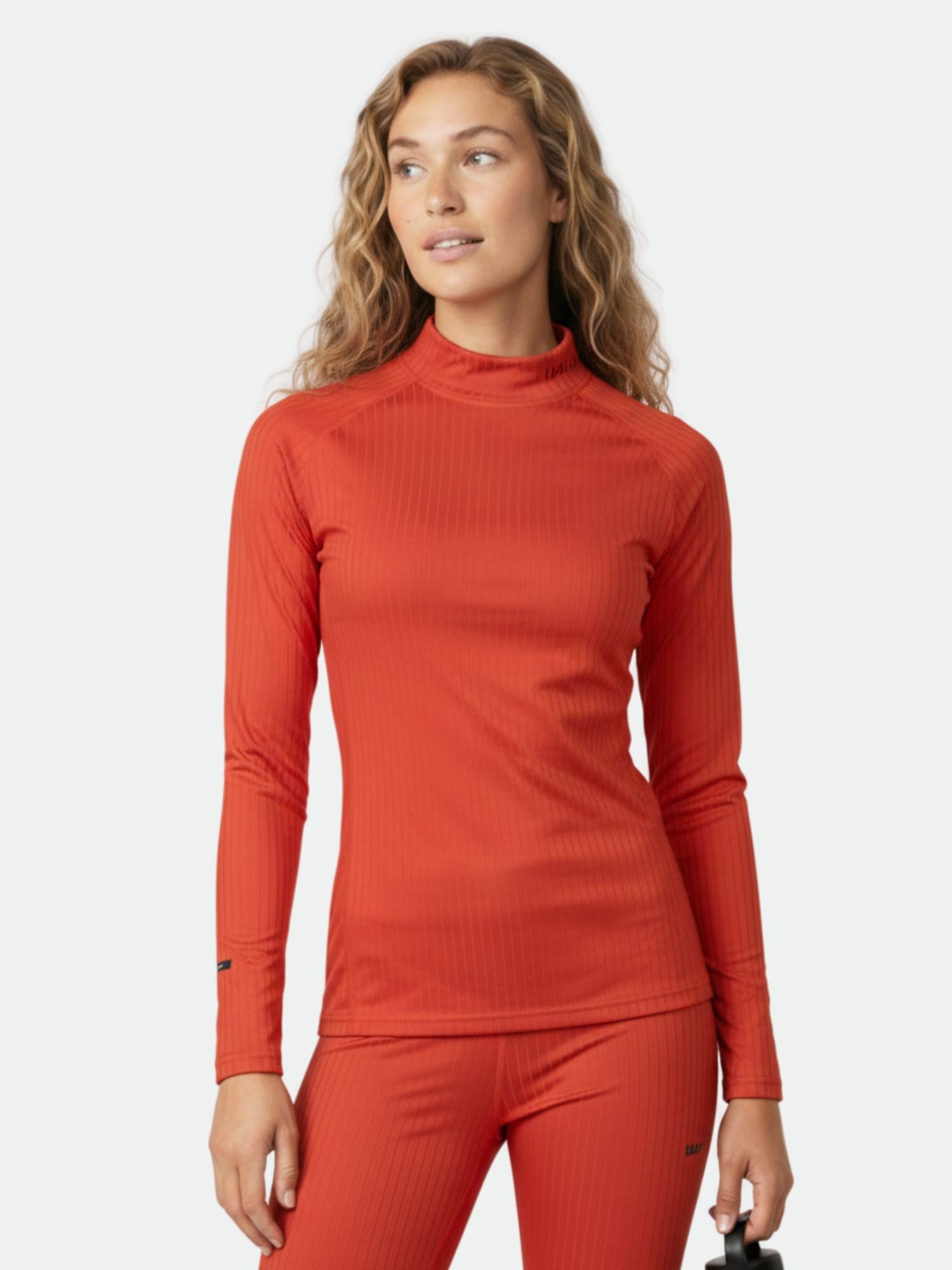 Eine Frau trägt das rote Halti Dual Baselayer Set Damen aus recyceltem Polyester vor einem schlichten Hintergrund.