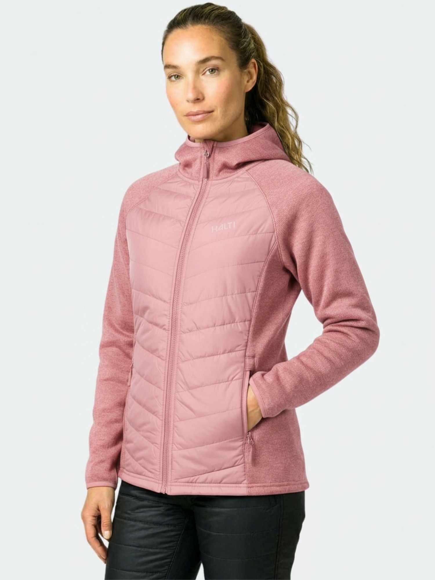 Frau in einer hellrosa Halti Streams Hybrid Midlayer Jacke Damen mit Händen in den Taschen, ideal für Outdoor-Aktivitäten.