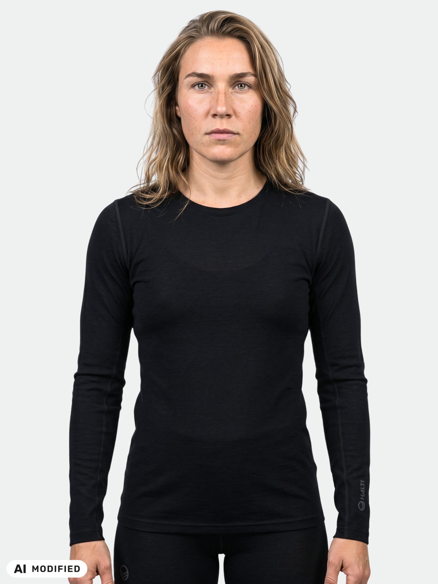 Eine Person mit langen, hellbraunen Haaren trägt ein schlichtes schwarzes „Halti Pihka II Merinowolle Shirt Damen“ vor einem neutralen Hintergrund.