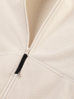 Nahaufnahme der Halti Soolo Midlayer Jacke Damen, teilweise geöffnet, zeigt cremefarbenes strukturiertes Gewebe und schwarzen Reißverschluss.