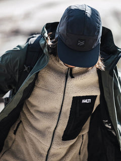 Person mit schwarzer Mütze, grüner Jacke und Halti Lumista Polar Fleece Jacke Herren, Blick nach unten.