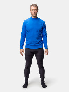 Ein Mann steht vorne und trägt das Halti Trone Fleece-Shirt Herren, eine schwarze Hose und Socken vor einem schlichten Hintergrund.