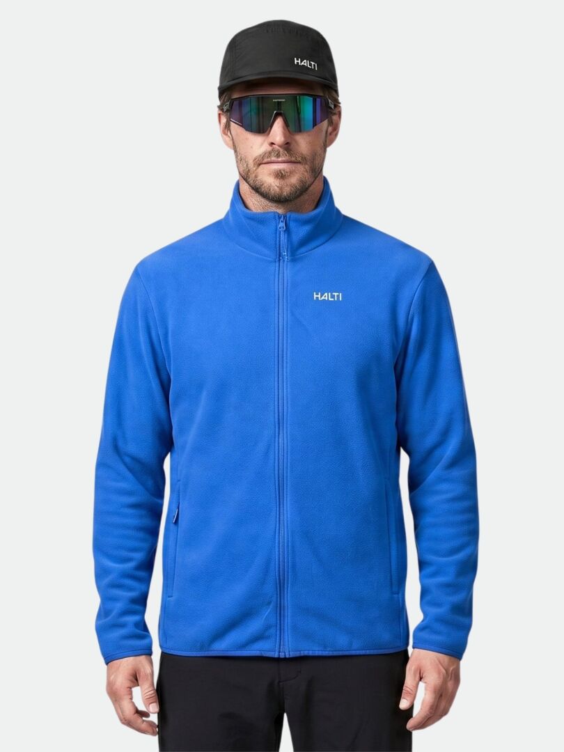 Ein Mann trägt eine Halti Rockmoon Fleecejacke für Herren als Zwischenschicht, dazu eine schwarze Hose, eine Mütze und eine reflektierende Sonnenbrille.