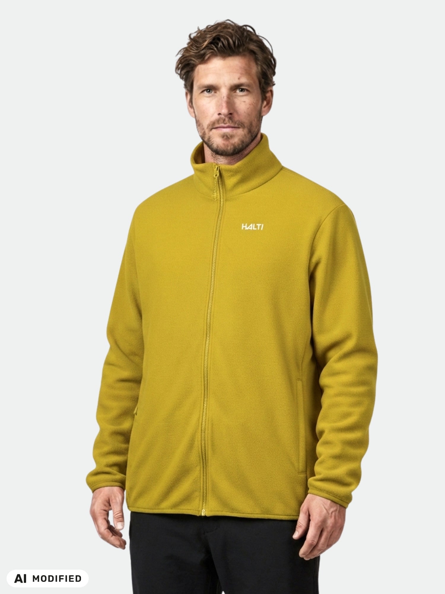 Ein Mann trägt die Halti Rockmoon Fleecejacke für Herren in Senfgelb und steht vor einem einfarbigen, hellen Hintergrund.