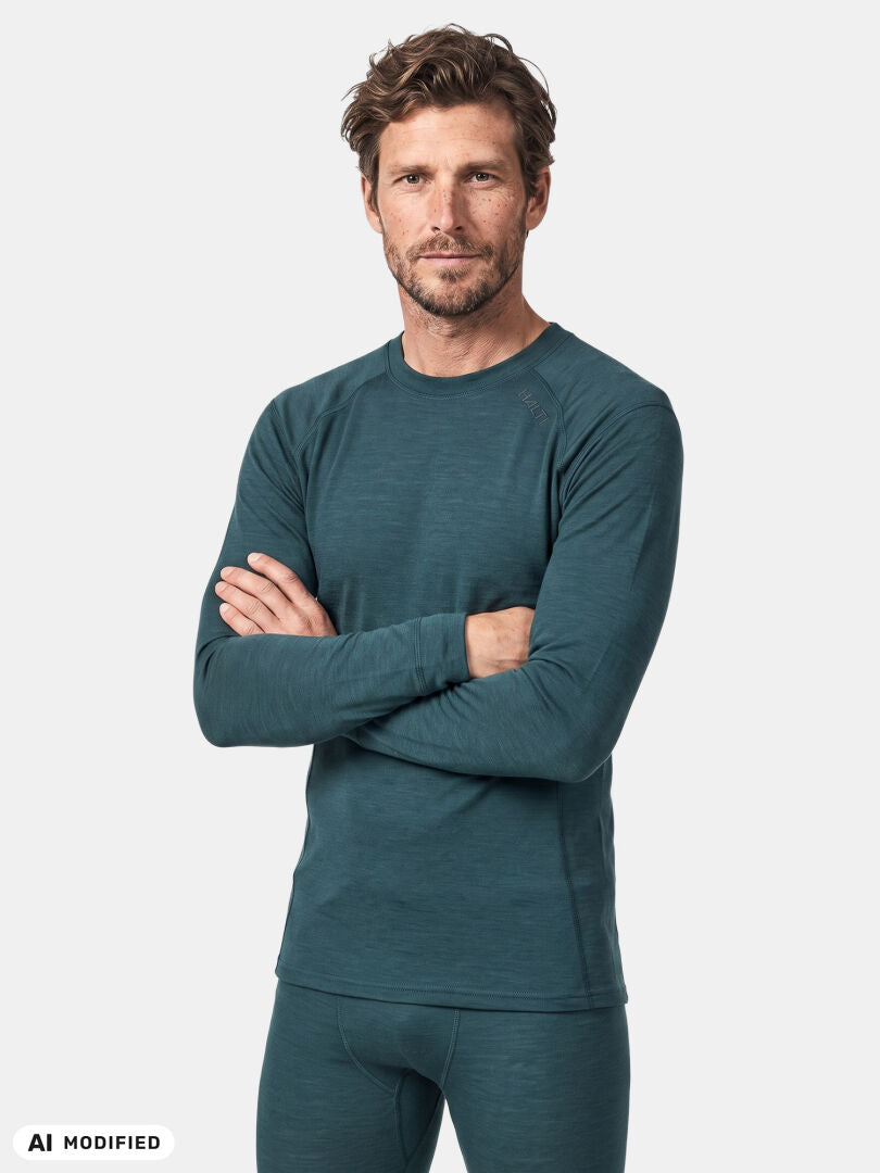 Ein Mann präsentiert das Halti Hossa II Merino-Unterwäsche-Set für Herren in der Farbe Teal, die Arme verschränkt, vor einem einfarbigen Hintergrund.