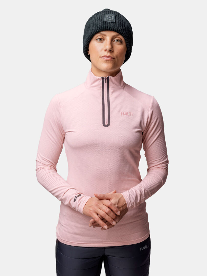 Eine Person in einem rosafarbenen Halti Jaako Hemd Damen und schwarzer Strickmütze steht mit verschränkten Händen.
