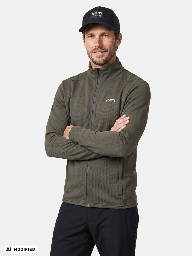 Ein Mann in einer olivgrünen Halti Kivikko Midlayer-Jacke und einer schwarzen Mütze steht mit verschränkten Armen vor einem einfarbigen Hintergrund.