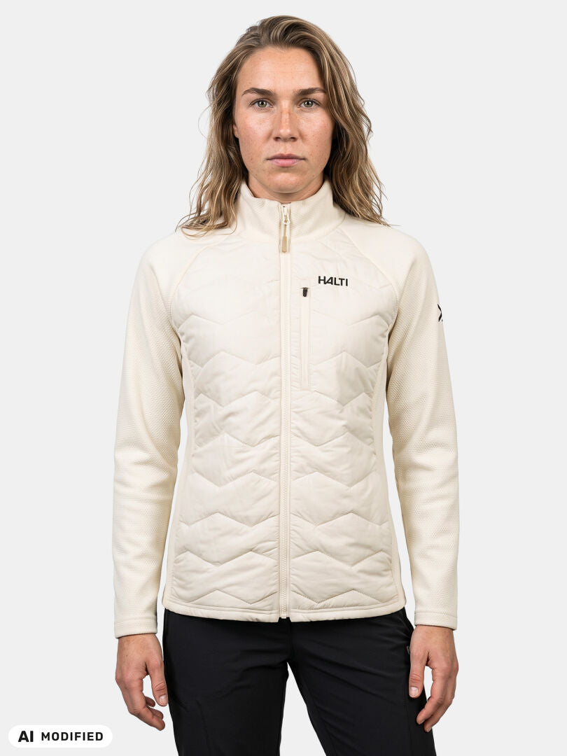 Eine Person, die eine cremefarbene „Halti Suomis Hybrid Layer Jacke Damen“ und eine schwarze Hose trägt, vor einem hellen Hintergrund.