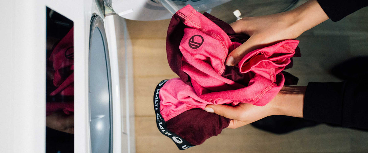 Eine Person, die rote und rosafarbene Sportkleidung in eine Frontlader-Waschmaschine gibt.