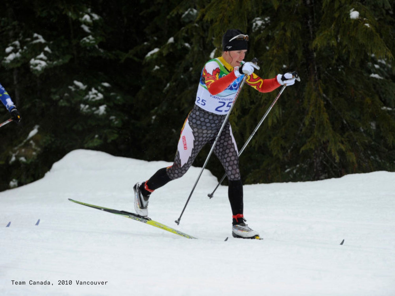 Skilangläuferin in einer Team-Kanada-Uniform beim Skifahren auf Schnee mit Bäumen im Hintergrund, Vancouver 2010.
