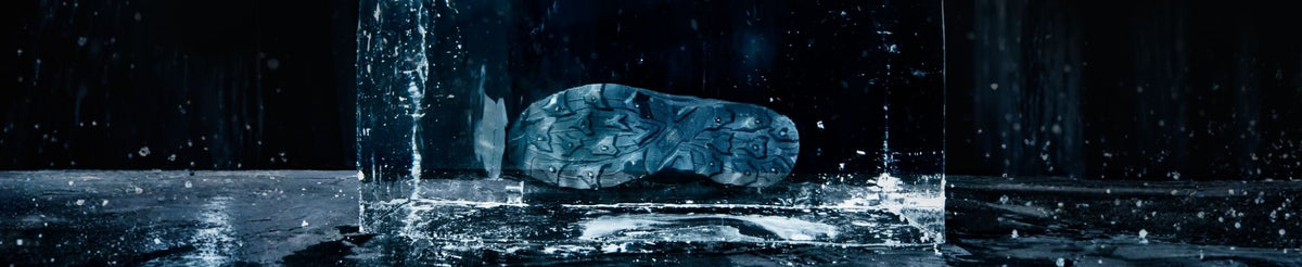 Ein dunkler Schuh ist in einem Eisblock vor einem schwarzen Hintergrund mit sichtbaren Wassertropfen eingeschlossen.