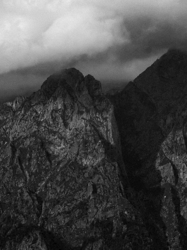 Schwarz-Weiß-Foto von zerklüfteten Berggipfeln mit Wolken, die die Gipfel teilweise verdecken.